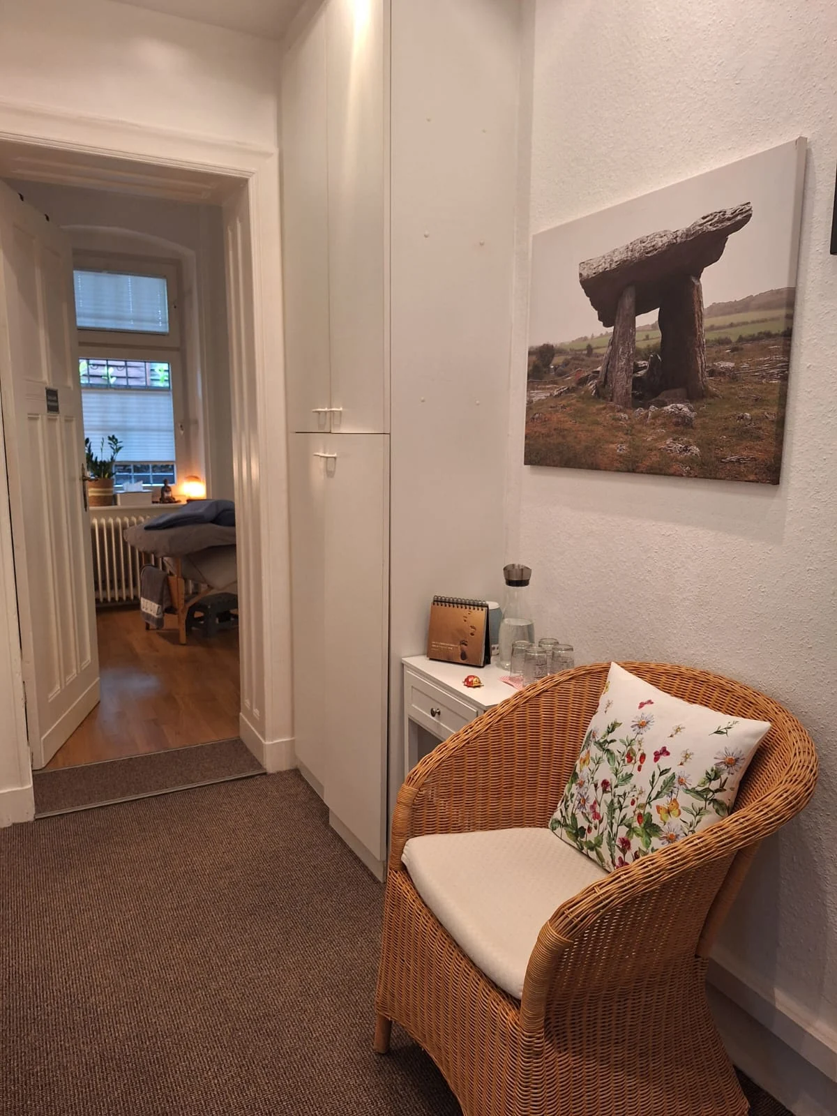 Wartebereich der Naturheilpraxis mit Korbsessel und Blick in den Behandlungsraum